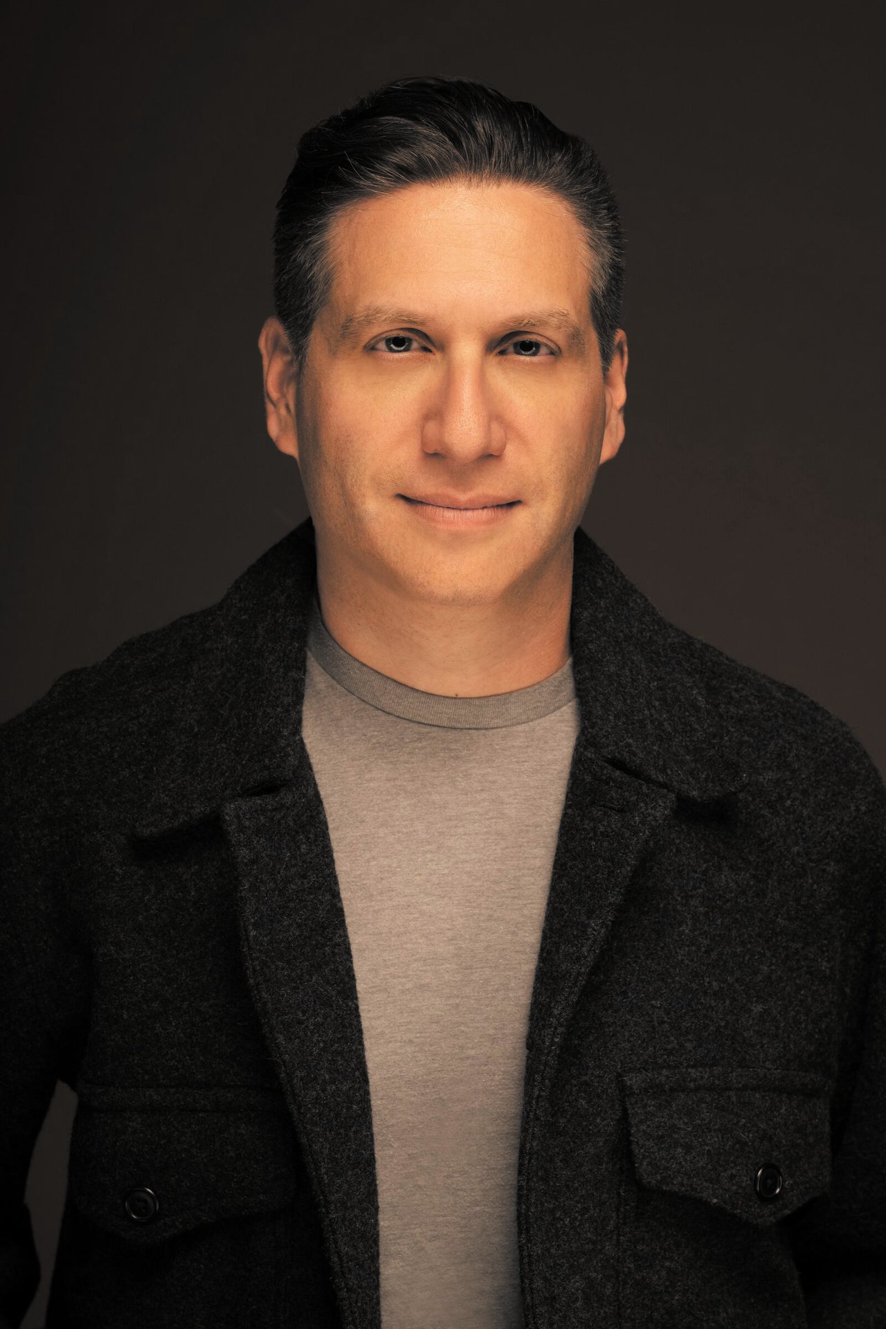 Shai Korman, smiling, in a warm-lit studio portrait